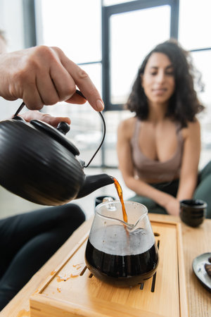 man pouring brewed puer tea into glass jug near middle eastern woman on blurred backgroundの写真素材