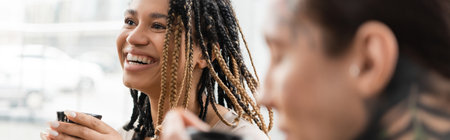 cheerful african american woman with dreadlocks holding Chinese cup with puer tea near tattooed man on blurred foreground, bannerの写真素材