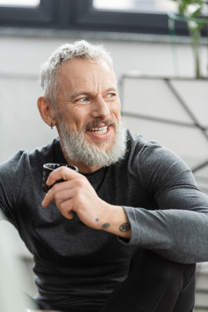 positive middle aged man with tattoos holding Chinese cup with puer tea in yoga studioの写真素材