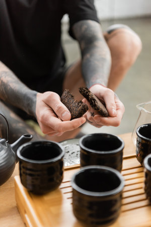 cropped view of tattooed man breaking compressed puer tea near traditional Chinese tea pot and cupsの写真素材