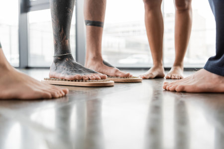 partial view of barefoot man with tattooed legs standing on nail board near peopleの写真素材