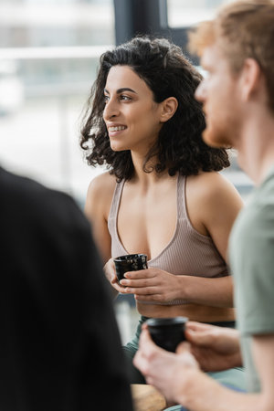 cheerful middle eastern woman with curly hair smiling during tea ceremony in yoga studioの写真素材