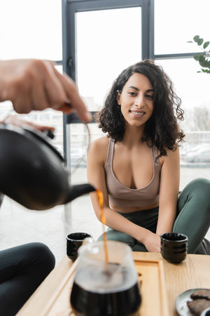happy middle eastern woman looking at man pouring puer tea into glass jugの写真素材