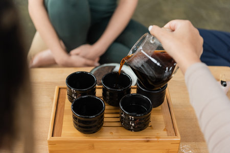 cropped view of woman pouring puer from glass jug into traditional tea cupsの写真素材