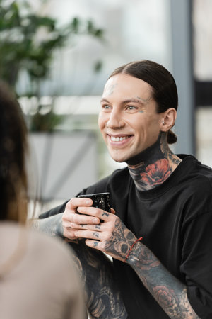 happy and tattooed man smiling while holding japanese cup with tea near woman on blurred foregroundの写真素材