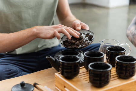 cropped view of man adding puer tea in traditional japanese teapot near cupsの写真素材