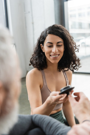happy middle eastern woman taking teapot lid near man on blurred foregroundの写真素材