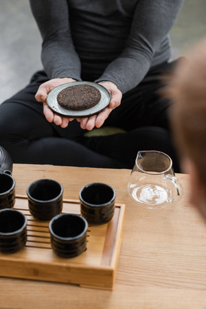 cropped view of man holding compressed puer tea near glass teapot and traditional tea cupsの写真素材