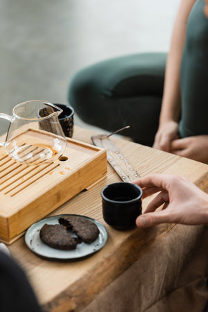 cropped view of man taking tea cup near fermented puer near glass jugの写真素材