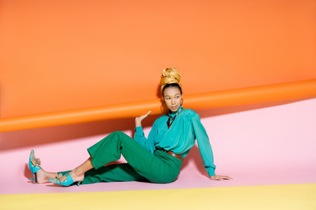 Pretty african american woman in summer outfit smiling while sitting on colorful backgroundの写真素材
