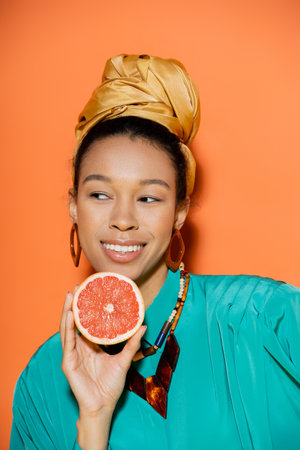Portrait of smiling and well dressed african american model holding grapefruit on orange backgroundの写真素材