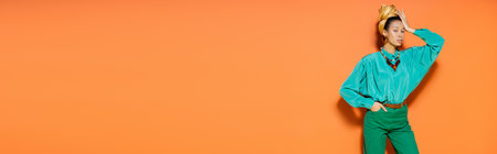 Well dressed african american woman in headscarf standing on orange background, bannerの写真素材
