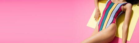 top view of cropped african american woman in colorful swimsuit getting tan on yellow and pink background, bannerの写真素材