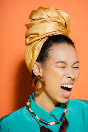 Stylish african american woman with headscarf screaming on orange backgroundの写真素材