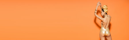 Side view of trendy african american woman in golden swimsuit on orange background, bannerの写真素材