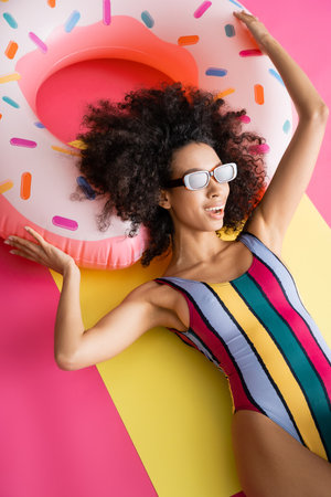 top view of positive african american model in striped swimwear and sunglasses getting tan near...