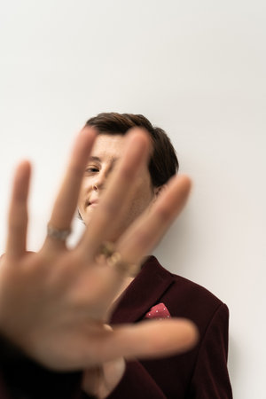 smiling woman in trendy blazer looking at camera through outstretched hand on grey background