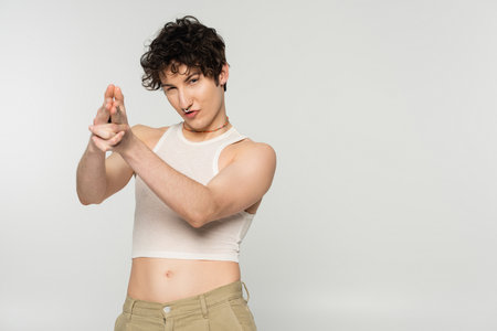 trendy nonbinary person looking at camera and showing finger gun gesture isolated on greyの写真素材