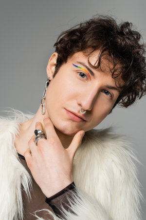 portrait of pansexual model with wavy brunette hair and rainbow eye liner looking at camera isolated on greyの写真素材