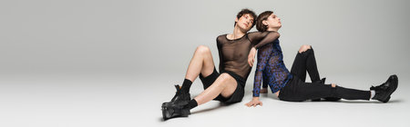 full length of young pangender models in stylish clothes sitting on grey background, banner