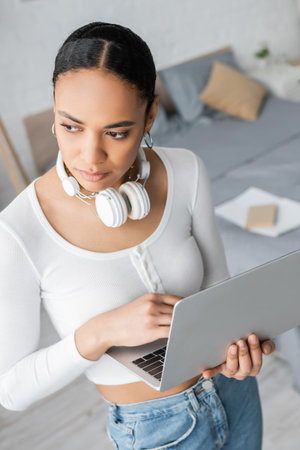 high angle view of young african american student with wireless headphones on neck holding laptopの写真素材