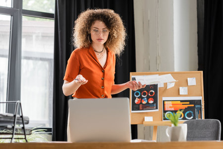 curly businesswoman in glasses doing online presentation during video call