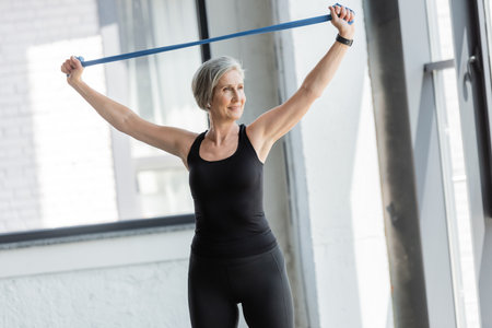 happy senior woman in black sportswear working out with resistance band above headの写真素材