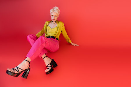 full length of blonde model in trendy clothes and heeled sandals posing on carmine pink backgroundの写真素材