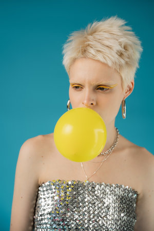 stylish albino woman with bare shoulders blowing bubble gum on blue backgroundの写真素材