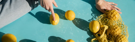 cropped view of woman sitting near string bag and ripe lemons on blue, bannerの写真素材