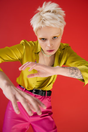 high angle view of albino woman with tattoo looking at camera while posing on carmine pink