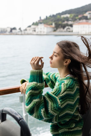 Side view of young woman in sweater standing near railing on yacht in Turkeyの写真素材