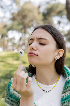 Focused young woman looking at daisy flower in blurred summer parkの写真素材