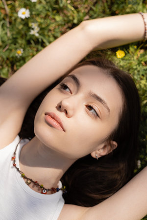Top view of young brunette woman lying on blurred lawn with flowers in parkの写真素材