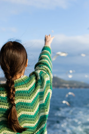 Back view of young woman in sweater outstretching hand and feeding blurred birds in Turkeyの写真素材
