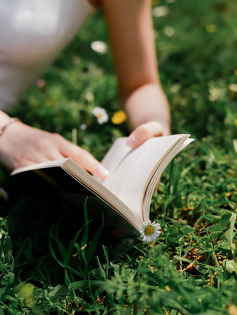 Cropped view of blurred woman holding book on meadow with daisiesの写真素材
