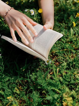 Cropped view of woman holding blurred book on lawn with flowersの写真素材