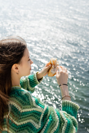 Side view of blurred brunette woman holding bread near blurred sea in Turkeyの写真素材