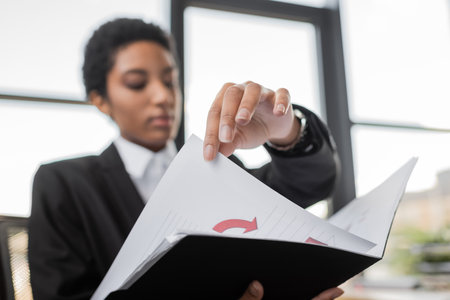 blurred african american businesswoman holding folder with infographics while working in officeの写真素材
