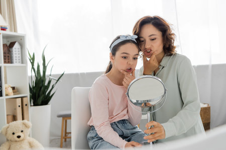 Pupil touching cheeks and looking at mirror near speech therapist in consulting roomの写真素材