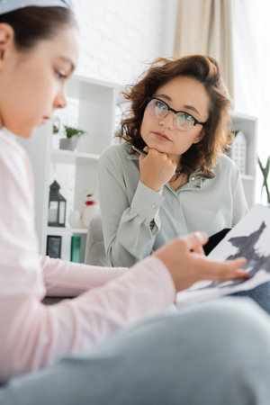 Psychologist holding pen near blurred child with Rorschach test in consulting roomの写真素材