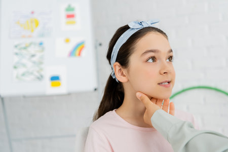 Speech therapist touching neck of preteen child during lesson in consulting room