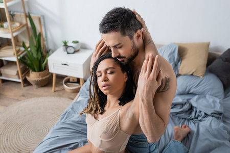 seductive african american woman with closed eyes near bearded shirtless man in bedroom at homeの写真素材