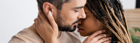 side view of bearded man and young african american woman with dreadlocks kissing at home, bannerの写真素材