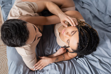 top view of passionate african american woman in lingerie and man in t-shirt embracing in bedroom at homeの写真素材