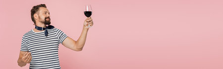 pleased man in striped t-shirt holding glass of red french wine isolated on pink, banner