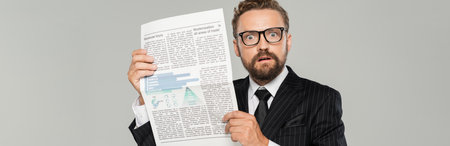 shocked businessman in suit and glasses holding newspaper isolated on grey, bannerの写真素材