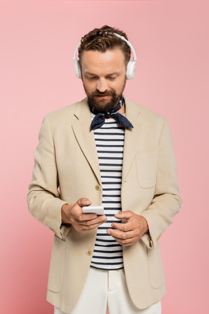 bearded french man in wireless headphones using smartphone isolated on pinkの写真素材