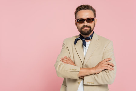 stylish french guy in neck scarf and sunglasses standing with crossed arms isolated on pinkの写真素材