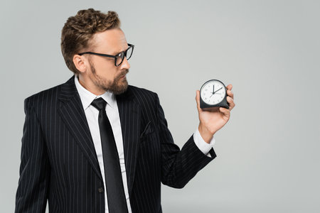 businessman in glasses and formal wear holding vintage alarm clock isolated on greyの写真素材